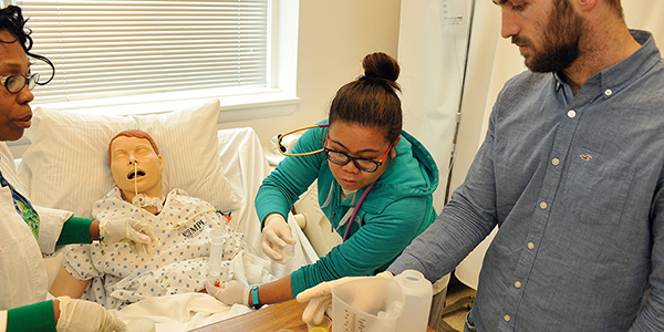 A professor supervising two nursing students during a hands-on simulation with a medical mannequin.